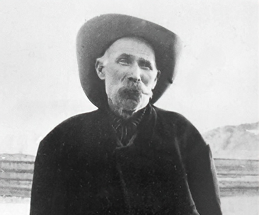 Montillus 'Old Man' Beatty in a wide-brimmed hat and heavy coat, standing in the open desert